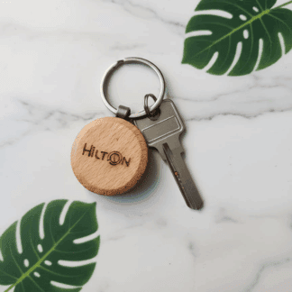 Personalized wooden round keychain with engraved "HILTON" and key attached.